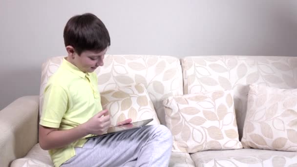 Kisfiú ül a kanapén, otthon tabletta — Stock videók