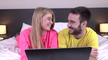çekici mutlu gülümseyen genç çift yatakta onlar sörf internet gibi bir dizüstü bilgisayar kullanarak onların pijama içinde dinlendirici