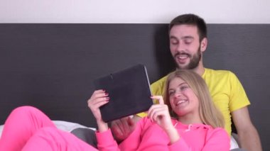 Yatakta gülümseyen çift tablette film izliyor