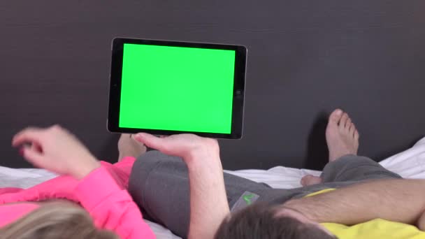 Sweet couple on bed watching something on white tablet gadget, green screen — Stock Video