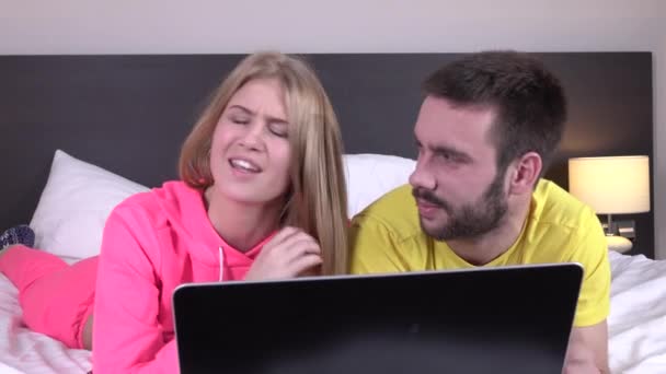 Молодая пара, используя ноутбук, лежа в постели дома, онлайн покупки — стоковое видео