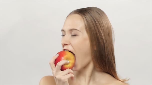 Chica rubia con frenillos comiendo manzana. Blanco. Primer plano. Movimiento lento — Vídeo de stock