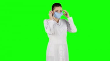 Kadın hemşire mavi tıbbi maske koyar. Yeşil ekran