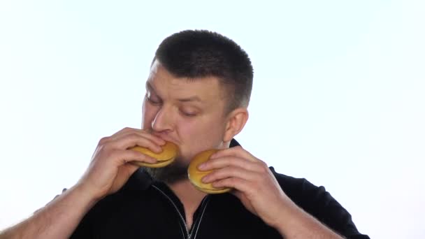 Young man eats a cheeseburgers. White. Slow motion — Αρχείο Βίντεο