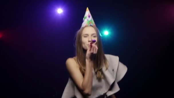 Дівчина дме конфетті з долонями, дме партійний свисток, танцює — стокове відео