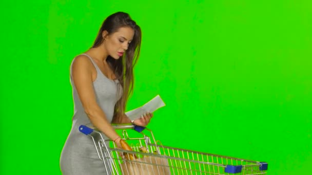 Donna che fa la spesa con il carrello al supermercato e controlla una lista cartacea. Schermo verde — Video Stock