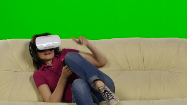 Женщина в очках виртуальной реальности играет в игру, сидя дома на диване. Зеленый экран — стоковое видео