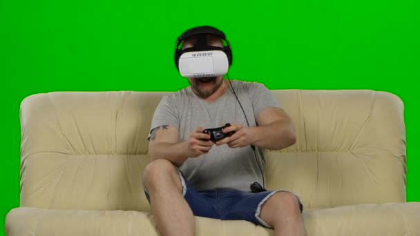 Человек в очках виртуальной реальности. Студийный снимок, белый диван. Зеленый экран — стоковое видео