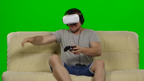 Young handsome man on sofa wearing VR headset glasses. Green screen — Stockvideo