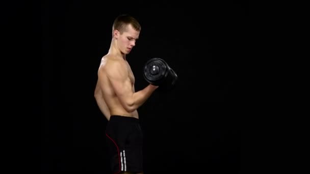 El hombre hace ejercicio bíceps con pesas en un gimnasio. Negro — Vídeos de Stock