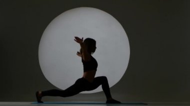 Kız ile bir bent-diz bacak germe yapıyor. Arka ışık. Siluet