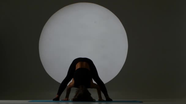 Woman stands on her head and changes the pose of legs. Back light. Silhouette — Stock Video