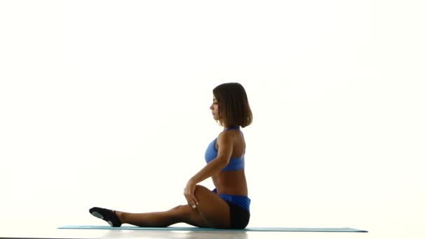 Atleta sentado no tapete de ioga e está esticando as pernas. Branco — Vídeo de Stock