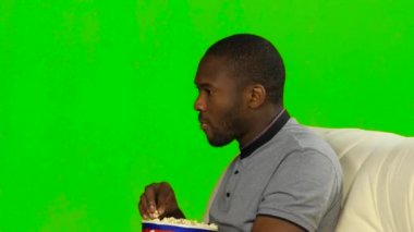 Adam kanepede oturan patlamış mısır yemek. Yeşil ekran