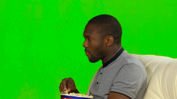 ソファーに座ってポップコーンを食べる男。緑色の画面 — ストック動画