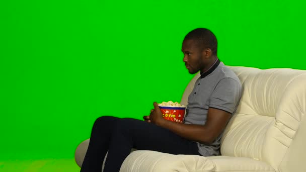 Hombre de piel oscura viendo televisión y comiendo palomitas de maíz. Pantalla verde — Vídeo de stock