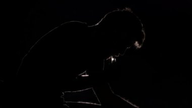 Acımasız üzgün adam oturur ve elektronik sigara içiyor. Siyah. Siluet