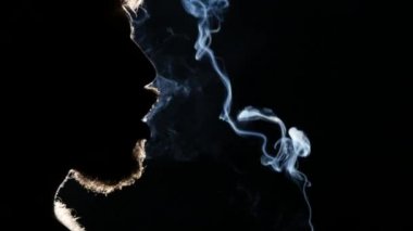 Adam bir puro içiyor. Büyük bir nefes alır ve duman puffs. Siyah ışık. Siluet. Yakın çekim