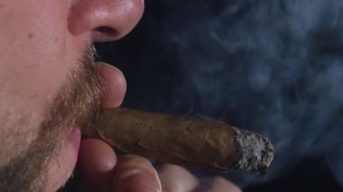 Adam bir puro içiyor. Büyük bir nefes alır ve duman puffs. Siyah. Yakın çekim