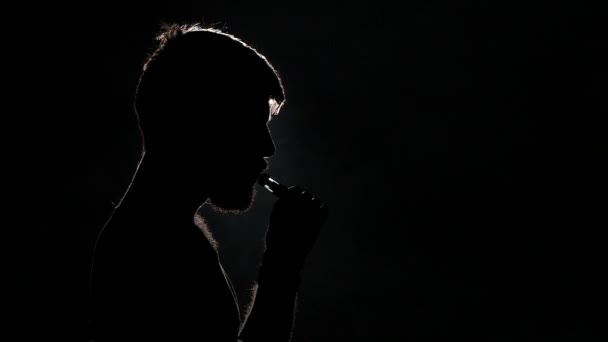 Το πορτρέτο ενός άντρα με γένια με ένα e-τσιγάρο. Μαύρο. Η σίλουονέτ. Κοντινό. Αργή κίνηση — Αρχείο Βίντεο