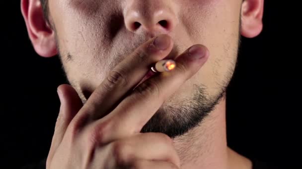 Un uomo con la barba leggera che fuma una sigaretta lunga. Nero. Chiudete. Rallentatore — Video Stock