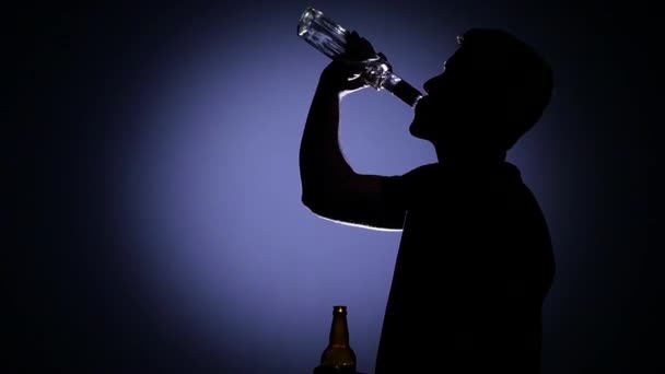 Man drinking from a bottle of vodka and then out of the bottle drinks beer. Back light. Slow motion — Stock Video