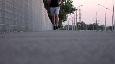 Gün batımında asfaltta parkta koşan bir koşucunun bacakları. Yavaş çekim