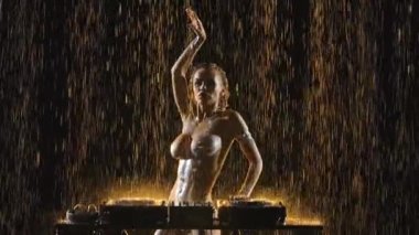 Seksi sarışın dans eder ve DJ konsolunda yağmur damlaları ve stüdyo ışıkları arasında müzik karıştırır. Kadınlar saçlarını dalgalandırır ve müzikten zevk alırlar. Disko ve moda etkinlikleri. Kapatın. Yavaş çekim.