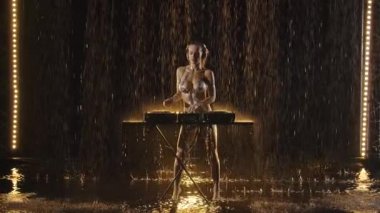 Parlak vücut boyalı çıplak sarışın DJ dans ediyor ve vinil bir pikapta karışık müzik çalıyor. Vücuda ve DJ konsoluna yağmur damlaları düşer. Çıplak parti. Yavaş çekim.