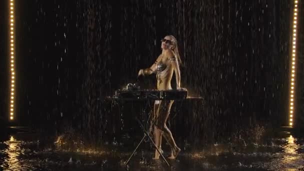 Hermosa hembra dj tocando música en la fiesta. Sexy rubia está bailando mientras disfruta de la música bajo la lluvia. Cuerpo desnudo mojado en gotas de agua. Movimiento lento. — Vídeos de Stock