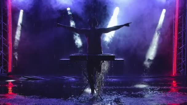Σιλουέτα ενός αρσενικού ντισκ τζόκεϊ που στέκεται πίσω από ένα μίξερ ήχου και παίζει μουσική με ένα ξυστό πίνακα σε ένα κλαμπ. Ο DJ χορεύει και κάνει διαφορετικές κινήσεις με τα χέρια του. Αργή κίνηση. — Αρχείο Βίντεο