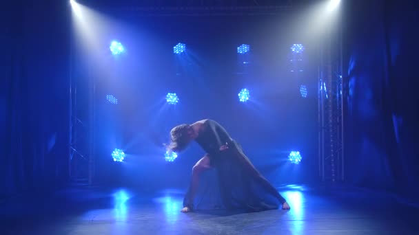 Прекрасная актриса танцует нежное чувственное презрение на черном фоне с синим подсветкой. Умелая молодая танцовщица в черном теле и юбке исполняет цепь современных танцевальных движений. Медленное движение. — стоковое видео