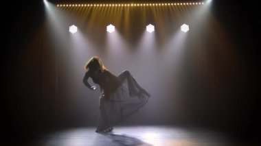 Siyah vücutlu ve etekli güzel bir aktris dumanlı arka plan ışıklı bir stüdyoda modern koreografinin nazik dans öğelerini sergiliyor. Siluet. Yavaş çekim.