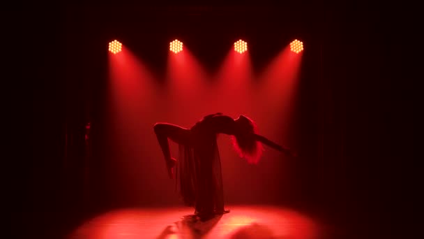 Jonge elegante vrouwelijke danser in zwart kostuum die contemp choreografie uitvoert in de rook van een dansstudio. Silhouet. Langzame beweging. — Stockvideo