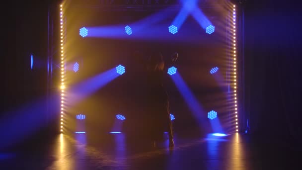 Silueta de elegante mujer delgada bailando coreografía contemp moderna sobre un fondo negro con luces azules. Una encantadora bailarina con un traje negro interpretando elementos acrobáticos de baile. Movimiento lento. — Vídeos de Stock