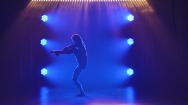 Çekici bir kadının silueti gölgelerde güzel bir şekilde dans ediyor mavi spot ışıklarıyla. Çağdaş bir performans sırasında akrobatik öğeler. Yavaş çekim.