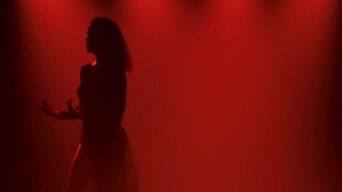 Karanlık bir stüdyoda kırmızı ışıklarla dans ederken modern düşünce dansı ve ince esnek bir dansçı. Siluet. Kapatın. Yavaş çekim.