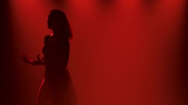 Modern koreografi tarzında esnek dans eden kadın. Bir bayan dansçı, mavi ışıklı dumanlı bir stüdyonun karanlığında enerjik dans figürleri sergiliyor. Yavaş çekim.