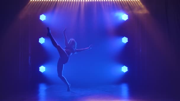 Silhouette of an attractive woman who is dancing a beautiful contemp in the shadows on a black background with blue spotlights. Acrobatic elements during a contemporary performance. Slow motion. — Stock Video