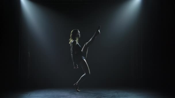 Ciemna sylwetka atrakcyjnej tancerki jest emocjonalnie wykonywana przez współczesną choreografię współczesną. Młoda kobieta w czarnym, odkrywającym garniturze tańczy z ekspresją w ciemnym, zadymionym studio. Zwolniony ruch — Wideo stockowe