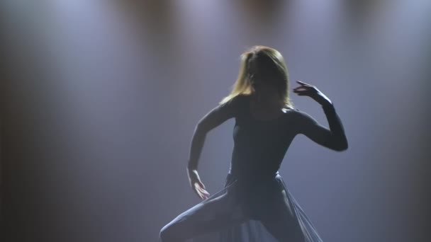 Современный современный балет, созерцание. Гибкая женщина выполняет акробатическую хореографию под прожекторами и курит на тёмном фоне. Силуэт. Закрывай. Медленное движение. — стоковое видео