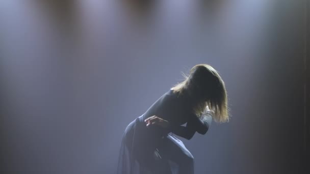 Ballet contemporáneo moderno, contemp. Mujer flexible realiza coreografía acrobática bajo focos y humo sobre un fondo oscuro. Silueta. De cerca. Movimiento lento. — Vídeos de Stock