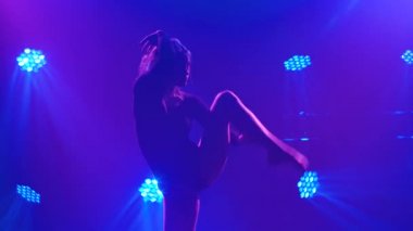 Siyah vücutlu çekici bir bayan dansçı sarı ışık demetleri altında dumanlı bir sahnede akrobatik tefekkür hareketleri yapıyor. Esnek, seksi bir kadının siluetleri. Yavaş çekim.