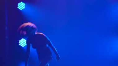 Profesyonel bir bayan dansçı mor ışıkla karanlık bir stüdyoda dans ederken dönüp zıplar. İnce bir vücudun silueti. Yaklaş. Yavaş çekim.