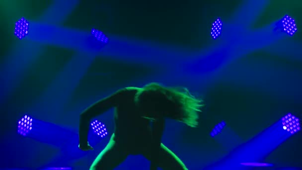 O dansatoare pasionată flexibilă practică elemente de dispreț într-un studio întunecat pe un fundal de reflectoare și fum. Silueta unei tinere femei atractive aproape. Slow motion . — Videoclip de stoc