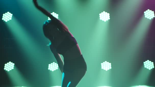 Una encantadora bailarina en un cuerpo negro interpretando elementos acrobáticos de danza contemp en un escenario ahumado bajo rayos de luz amarilla. Siluetas de mujer sexy flexible de cerca. Movimiento lento. — Vídeo de stock