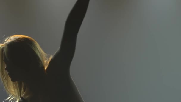 Una silhouette di una donna flessibile che si esibisce in elementi di danza al crepuscolo. Elegante donna che balla disprezzo in uno studio fumoso buio con retroilluminazione. Al rallentatore. Da vicino.. — Video Stock
