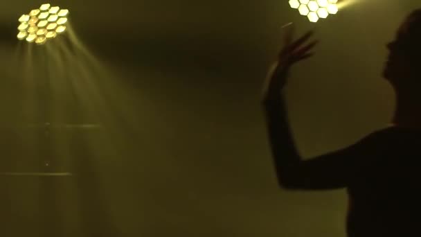 Danse moderne impulsive du mépris avec des éléments acrobatiques exécutés par une jeune femme flexible. La danseuse apprécie la danse et s'envole dans un studio sombre avec des lumières jaunes. Silhouette en gros plan. Mouvement lent. — Video