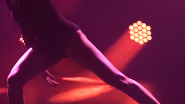 Silhouet van een fitte vrouw die een prachtige contemp danst in de schaduw op een zwarte achtergrond met gekleurde spots. Acrobatische elementen tijdens een moderne show. Benen dicht. Langzame beweging. — Stockvideo