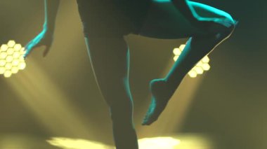Siyah bluzlu ve şortlu genç bir kadın dramatik aşağılama danslarında ya da modern balede sahnede dans ediyor. İnce bir bedene ışık huzmelerinde yaklaş. Yavaş çekim.
